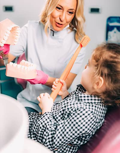 Dentist Teaching Child How To Brush Teeth With Model