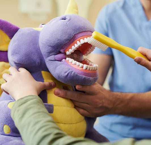 Pediatric Dentist Teaching Child Brushing With Dragon Toy